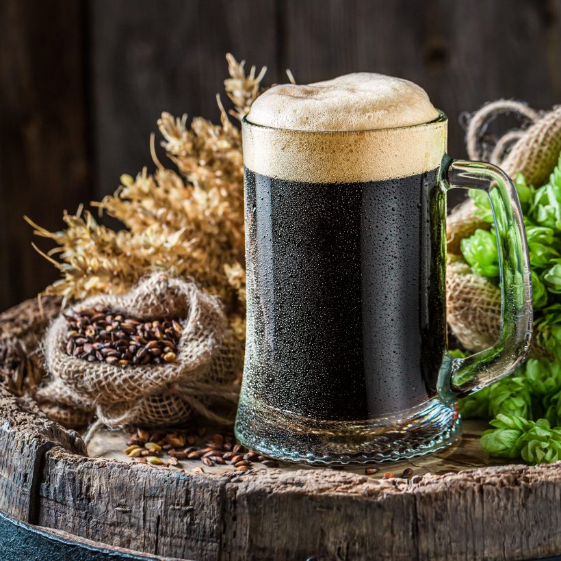 Dark beer with foam. Brewing industry. Dark beer on wooden barrel.
